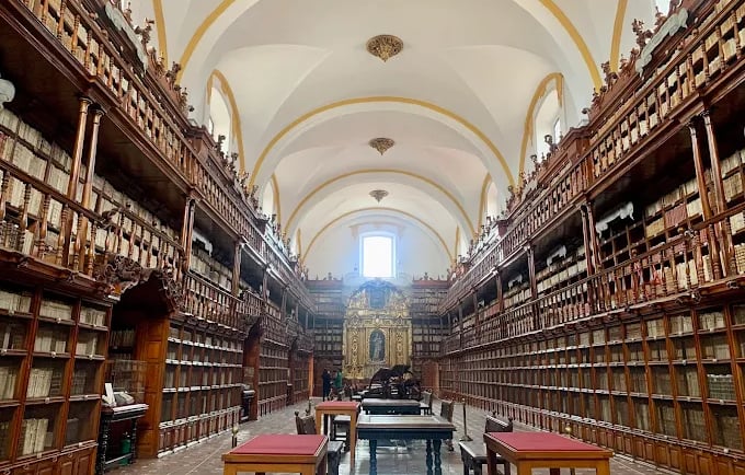 Historic university library with ornate wooden bookshelves and vaulted ceilings.