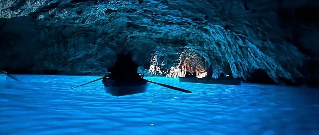 Small rowboats exploring the stunning Blue Grotto sea cave in Capri, Italy, with vibrant blue illuminated water.