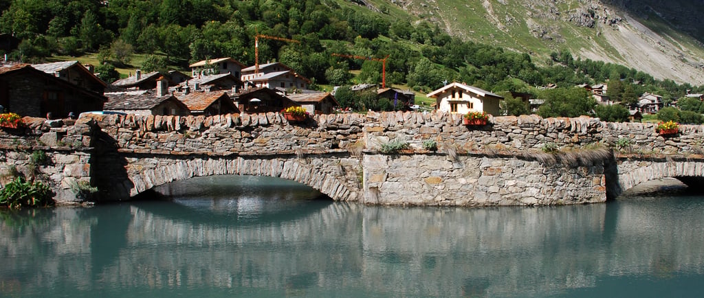 Historic stone arch bridge over a turquoise alpine river in a scenic mountain village.