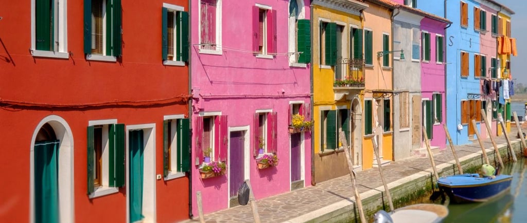 Colorful houses along a canal in Burano Venice with small boats docked in the water.