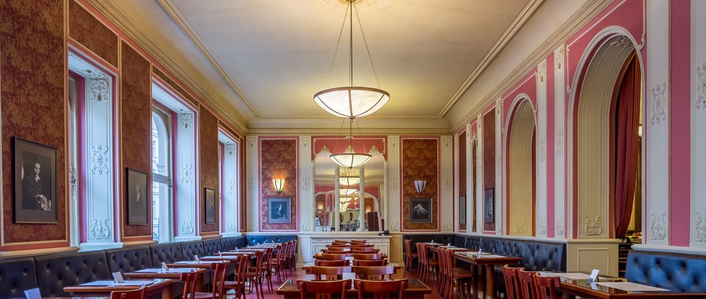 Elegant restaurant interior with red patterned wallpaper, luxury dining tables, and ornate white molding.