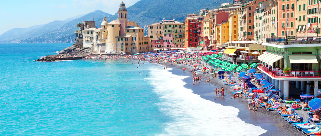Sunny view of Camogli beach in Liguria, Italy, with colorful houses and turquoise Mediterranean waters.