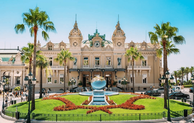 The historic Monte Carlo Casino in Monaco with a fountain and palm trees under a blue sky.