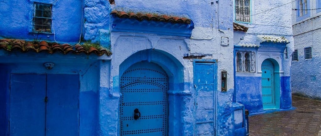 Narrow street in Chefchaouen, Morocco, featuring traditional blue painted walls and arched doors.