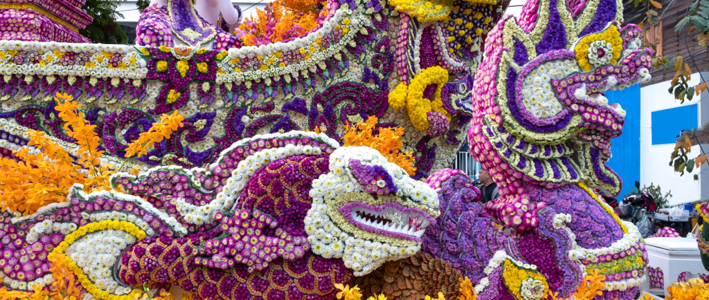 Intricate flower festival float featuring colorful Naga dragon sculptures made of purple and yellow blossoms.