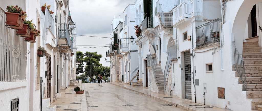 Narrow stone street lined with traditional white houses in a scenic Italian village in Puglia.