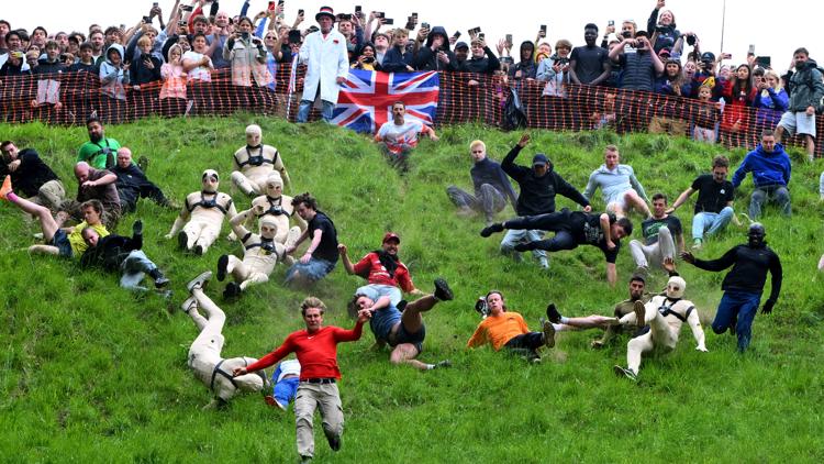 Crowds of people tumbling down a steep green hill during the annual Cooper's Hill Cheese-Rolling competition.