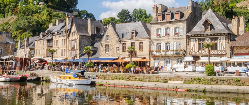 Scenic waterfront with historic stone houses and outdoor cafes in Dinan, Brittany, France.