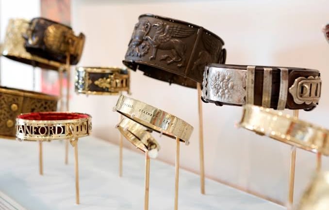 A collection of antique leather and metal dog collars with intricate engravings displayed on stands.