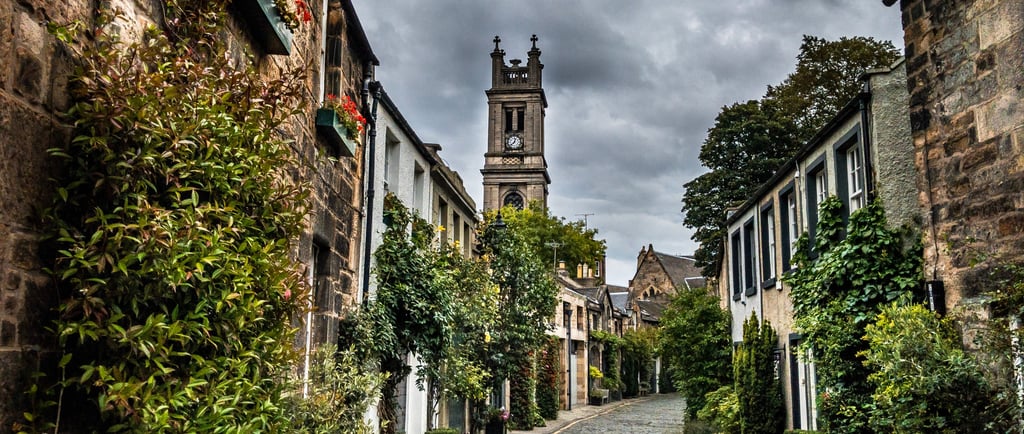 Historic cobblestone street in Edinburgh's Circus Lane with stone houses and St Stephen's Church tower.