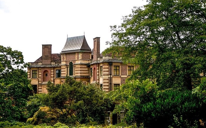 Historic Eltham Palace art deco mansion architecture nestled behind lush green garden trees in London.
