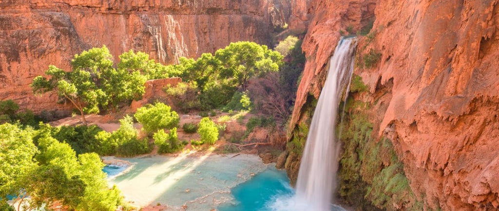 Havasu Falls in the Grand Canyon with turquoise water and red rock cliffs at sunrise.