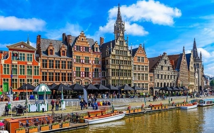 Historic medieval guild houses along the Graslei canal in Ghent, Belgium under a sunny blue sky.