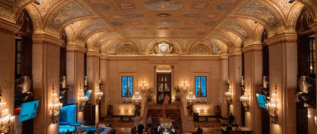 Elegant historic hotel lobby with ornate painted ceilings, gold chandeliers, and a grand marble staircase.