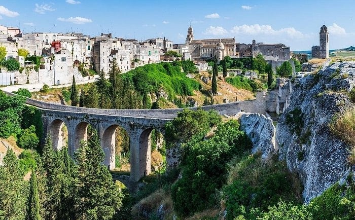 Ancient stone bridge and historic white buildings in the scenic ravine town of Gravina in Puglia, Italy.