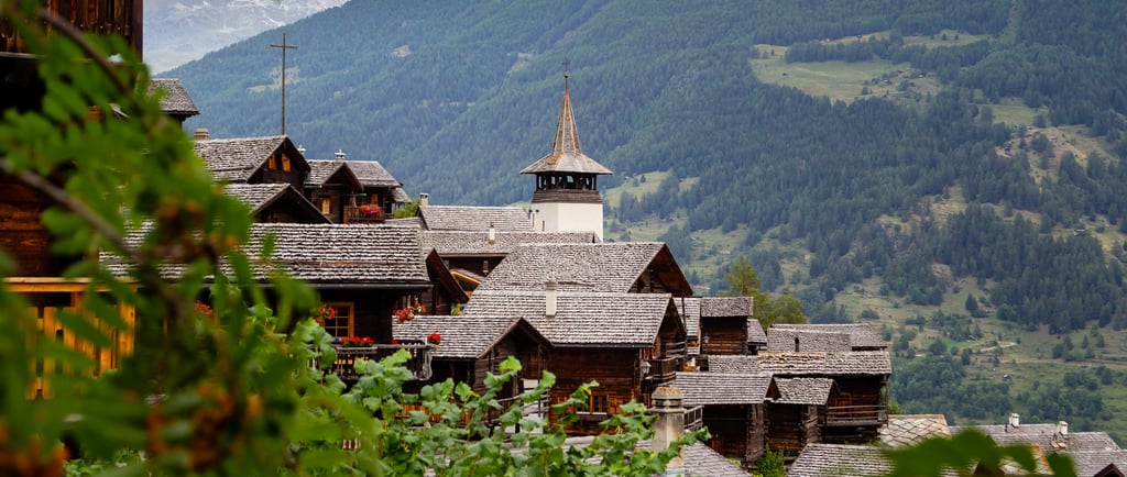 Rustic wooden chalets and a church steeple in a traditional Swiss mountain village.