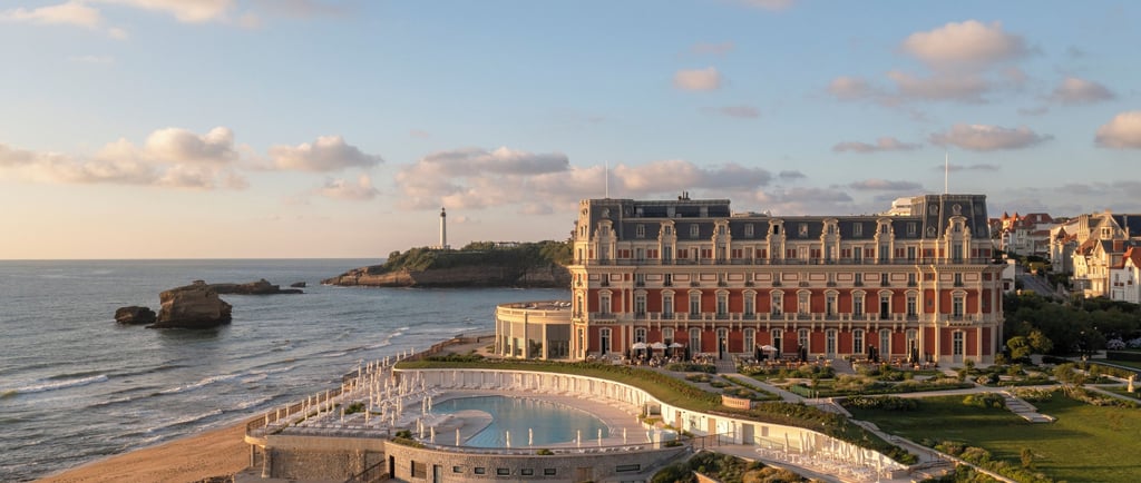 Luxury Hôtel du Palais in Biarritz at sunset with a view of the pool, beach, and Phare de Biarritz lighthouse.
