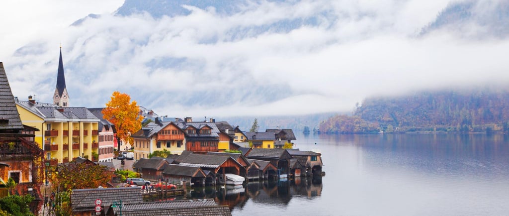 Scenic lakeside village of Hallstatt, Austria, with mist-covered mountains and traditional wooden boathouses.