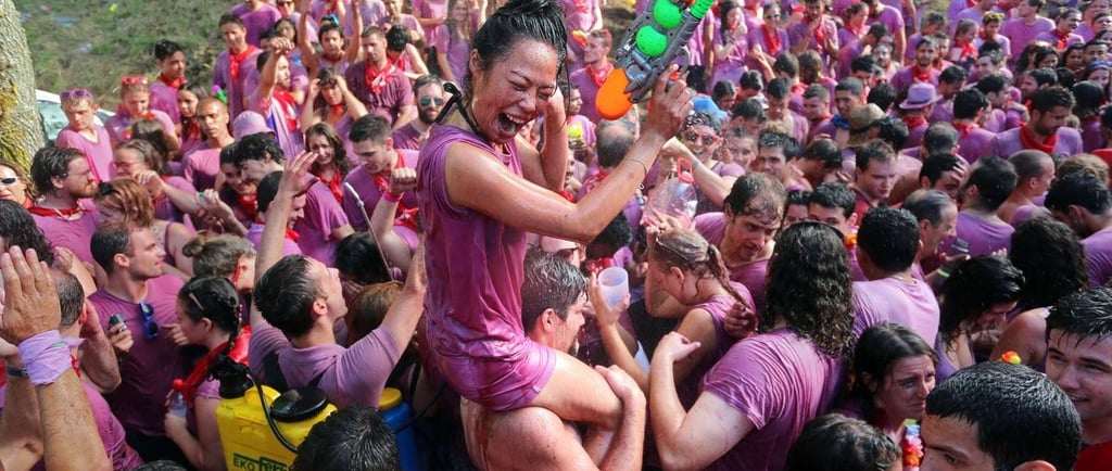Crowd of people celebrating the Haro Wine Fight festival in Spain with purple wine-soaked clothes and water guns.