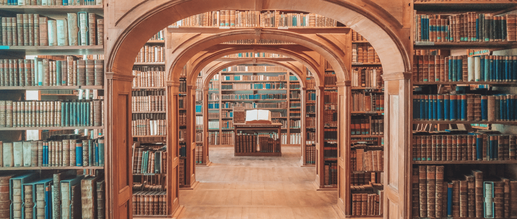Ancient library interior with symmetrical wooden arches and shelves filled with vintage leather-bound books.