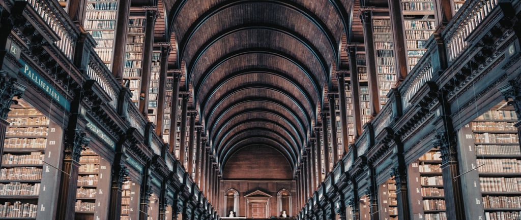 The historic Long Room at Trinity College Dublin library featuring high vaulted ceilings and wooden bookshelves.