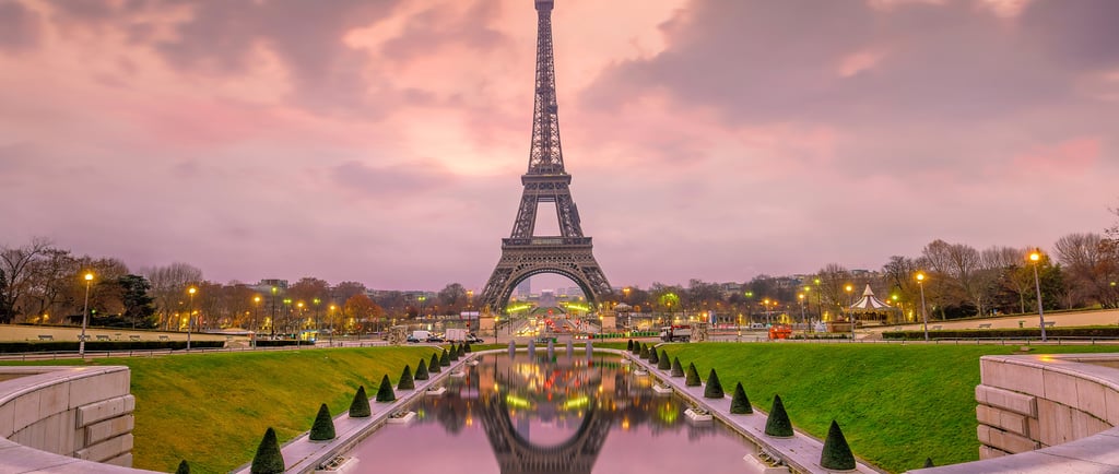 The Eiffel Tower at sunset with pink clouds reflected in the Trocadero Gardens fountain in Paris.