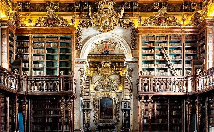The ornate Baroque interior of the Joanina Library in Coimbra, Portugal, featuring gilded wood bookshelves.