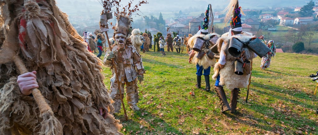 Participants in traditional European pagan carnival costumes with burlap, cowbells, and birch bark masks in a field.