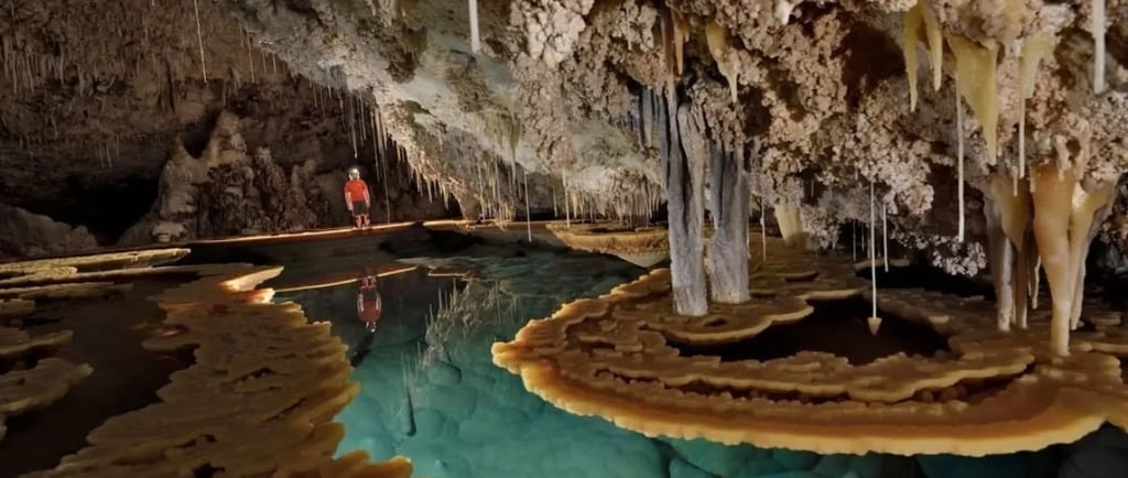 A lone adventurer explores an ancient cave with stunning stalactites, stalagmites, and crystal-clear turquoise water