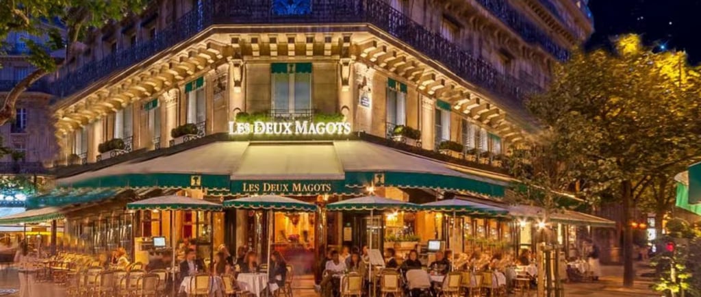 The illuminated exterior of Les Deux Magots cafe in Paris with outdoor terrace seating at night.