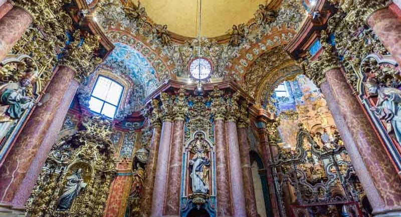 Ornate gold and marble interior of a Spanish Baroque church with intricate sculptures.