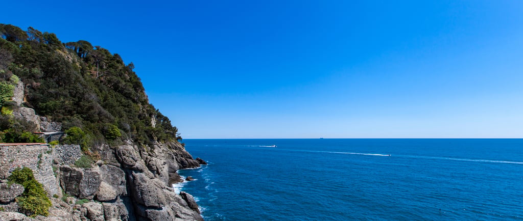 Panoramic view of steep rocky cliffs and the deep blue Mediterranean Sea under a clear sky in Portofino, Italy.