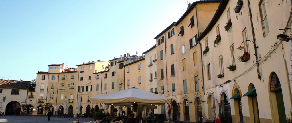Historic Piazza dell'Anfiteatro in Lucca with yellow buildings and outdoor cafe seating.
