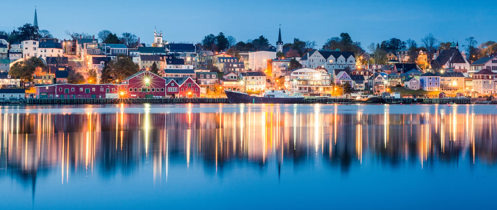 A panoramic night view of Lunenburg harbor with colorful buildings reflecting in the calm water.