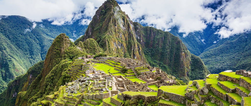 Ancient Inca ruins of Machu Picchu nestled in the green Peruvian Andes mountains under a cloudy sky.