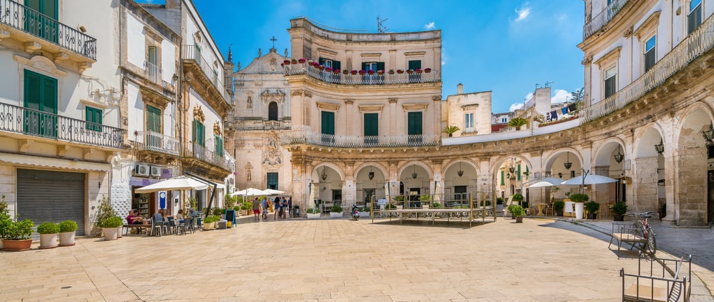 Sunny view of Piazza Maria Immacolata in Martina Franca, Italy, featuring historic Baroque architecture and cafes.