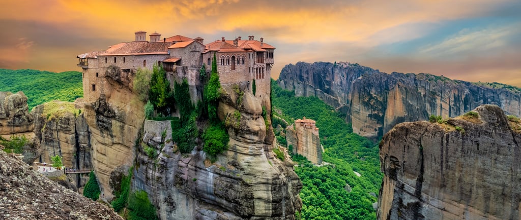 Ancient Meteora monasteries perched on steep rock cliffs in Greece during a vibrant sunset.