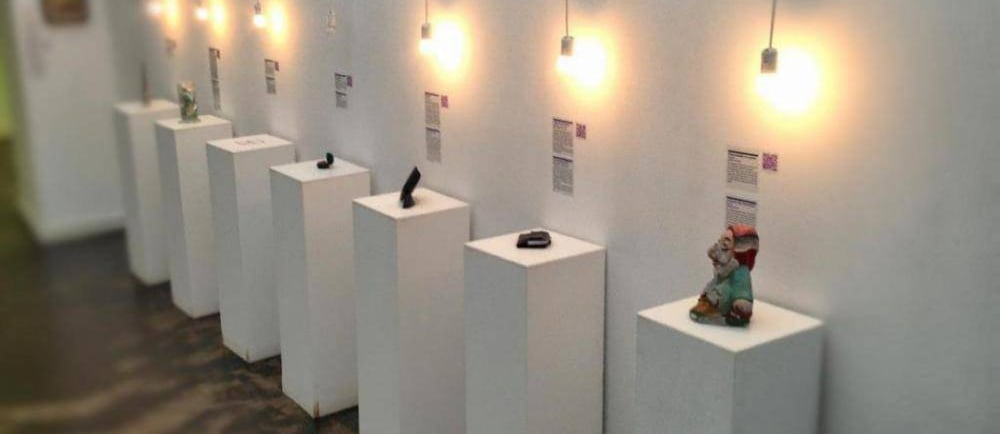 Modern art gallery exhibition featuring small sculptures on white pedestals under hanging pendant lights.