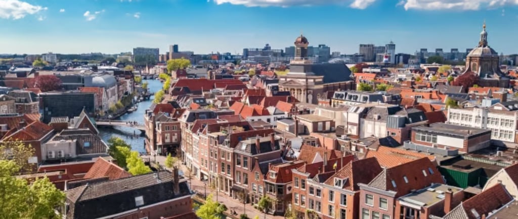Aerial view of Leiden city center featuring traditional Dutch architecture, canals, and historic churches under a blue sky.