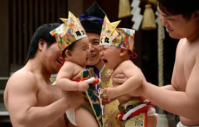 Two crying babies wearing paper crowns compete in a traditional Japanese Nakizumo baby crying contest.