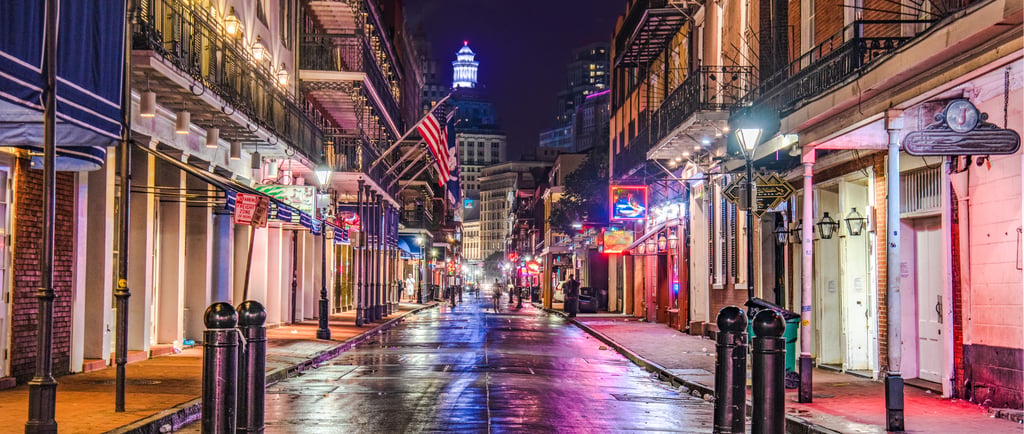 Neon lights reflect on the wet pavement of Bourbon Street in the New Orleans French Quarter at night.