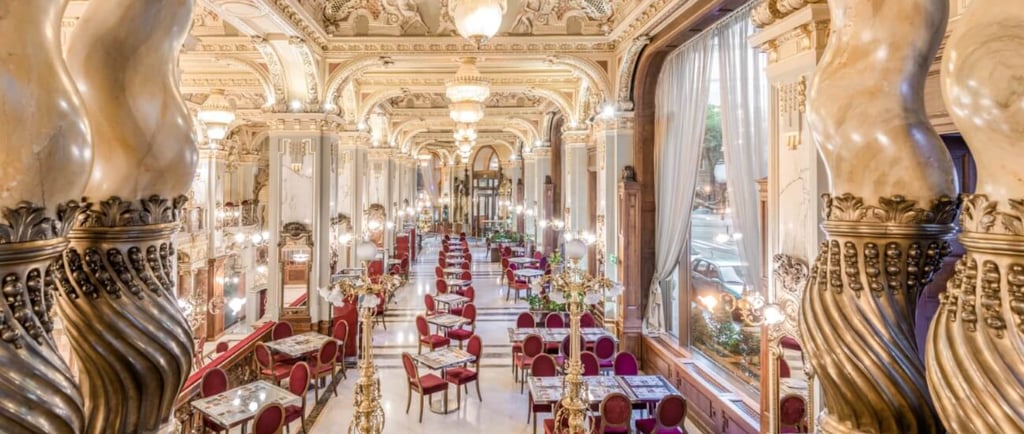 Elegant New York Cafe interior in Budapest with ornate gold ceilings, marble columns, and red velvet chairs.
