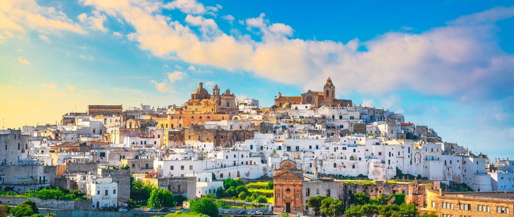 Panoramic view of Ostuni, the White City in Puglia, Italy, featuring historic whitewashed buildings and a blue sky.