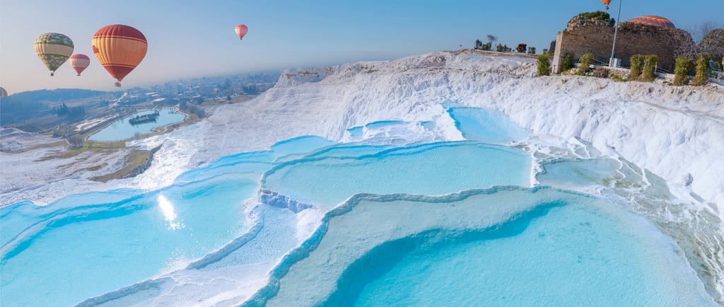 Colorful hot air balloons flying over the blue thermal pools and white travertine terraces of Pamukkale, Turkey.