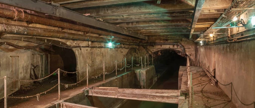 Underground sewer tunnel with concrete arches, old metal pipes, and industrial infrastructure.
