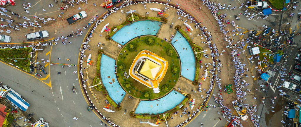 Aerial view of a Phuket Vegetarian Festival parade circling a city roundabout with crowds in white.
