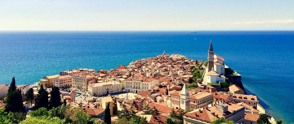 Elevated view of Piran, Slovenia, a historic coastal town with terracotta rooftops, a bell tower, and lush green trees