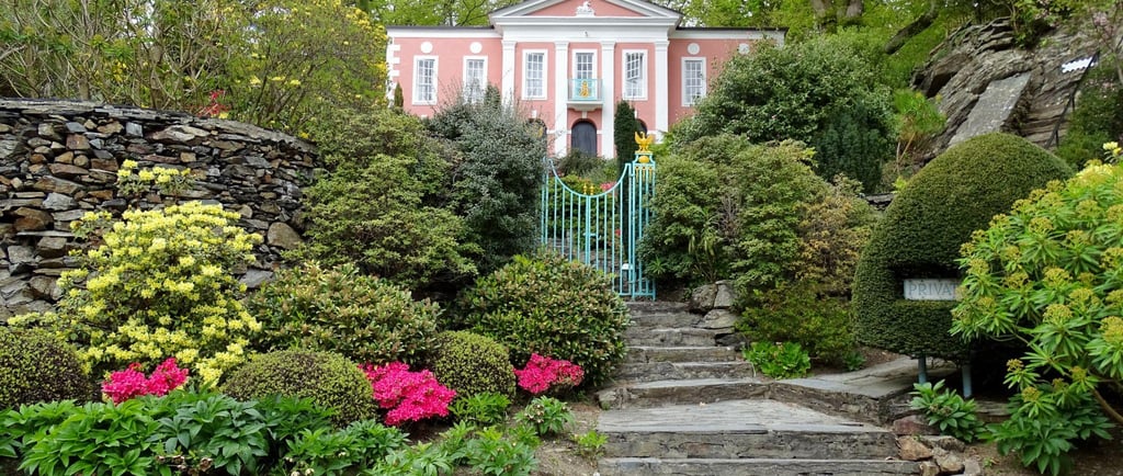 Stone steps leading to a pink Georgian house in Portmeirion Village surrounded by lush green gardens.