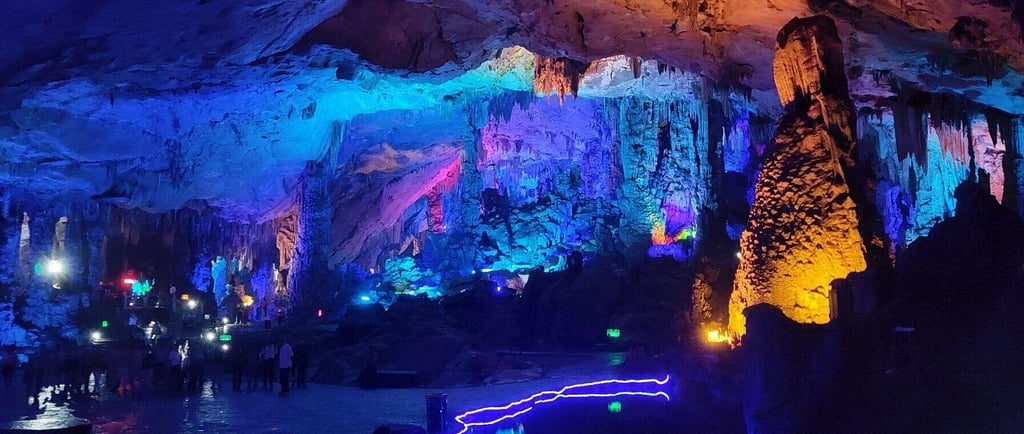 A limestone cave with colorful LED lighting illuminating stalactites and stalagmites.