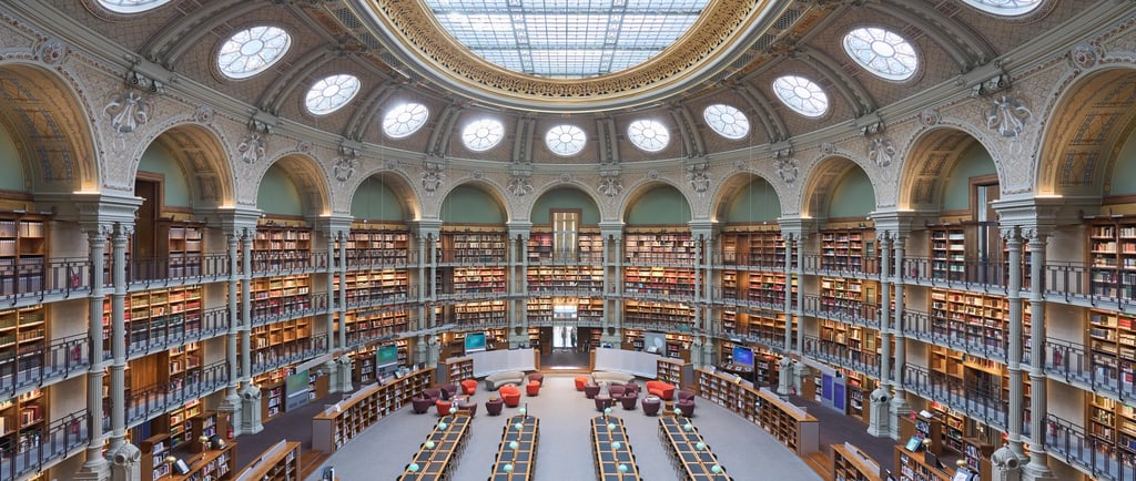 The historic circular reading room at the Richelieu Library in Paris featuring a glass dome and tiers of bookshelves.
